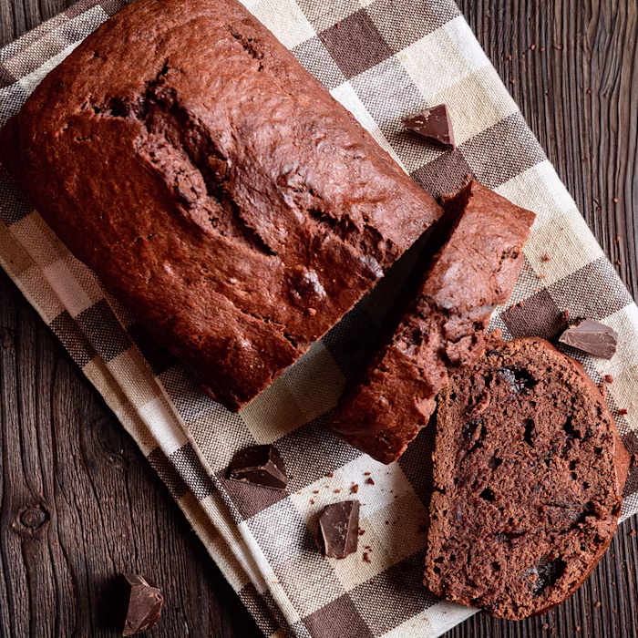 A partially sliced loaf of chocolate banana buttermilk cake on a tea towel