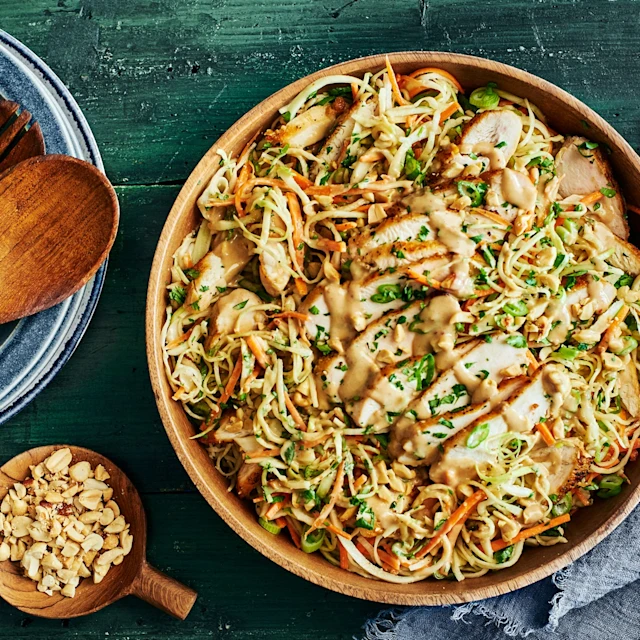 A plate of cabbage and chicken salad with a bowl of peanut