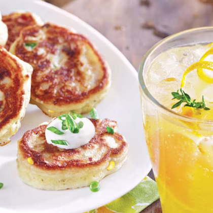 A plate of mini-pancakes with bacon, cheddar goat cheese and corn with a glass of juice