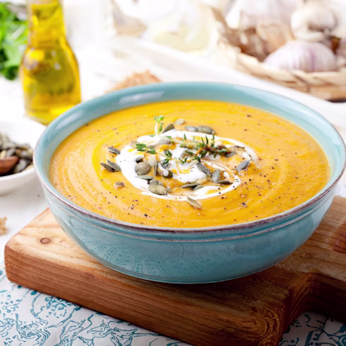 A bowl of roasted butternut squash soup, garnished with cream and herbs