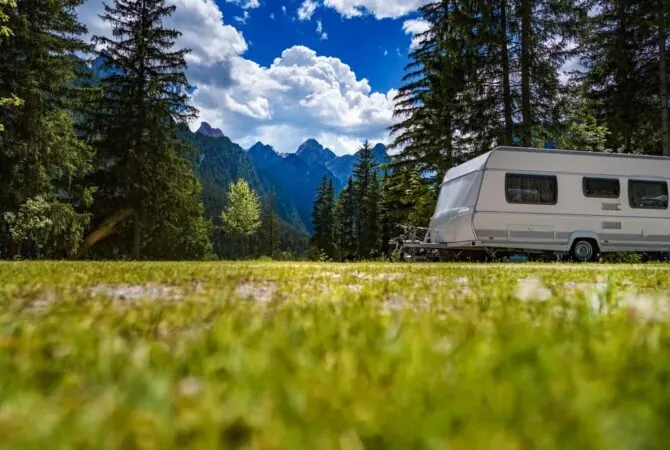 A trailer in an open field with trees and mountains in the background.