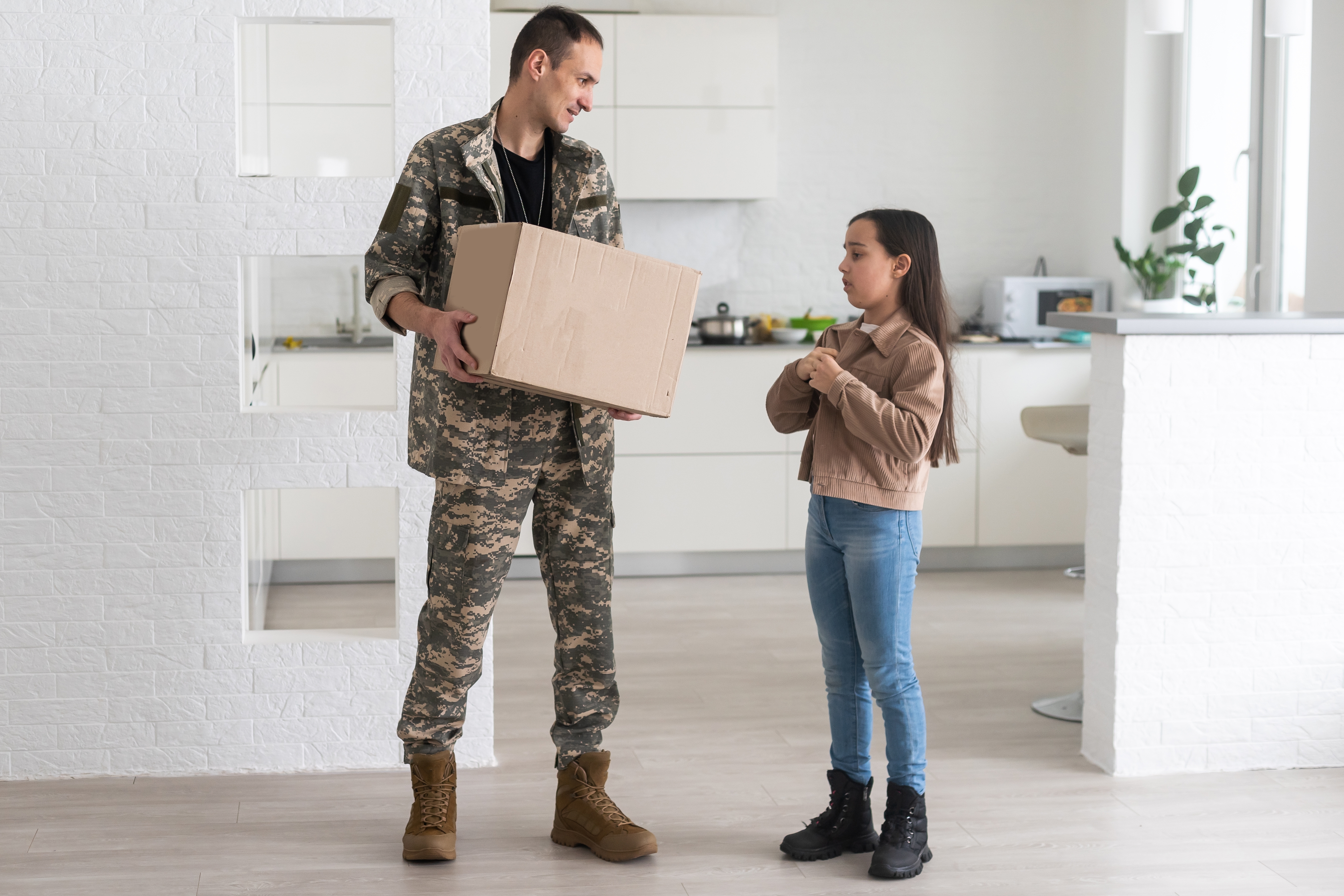A man holding a box facing a girl standing in a kitchen