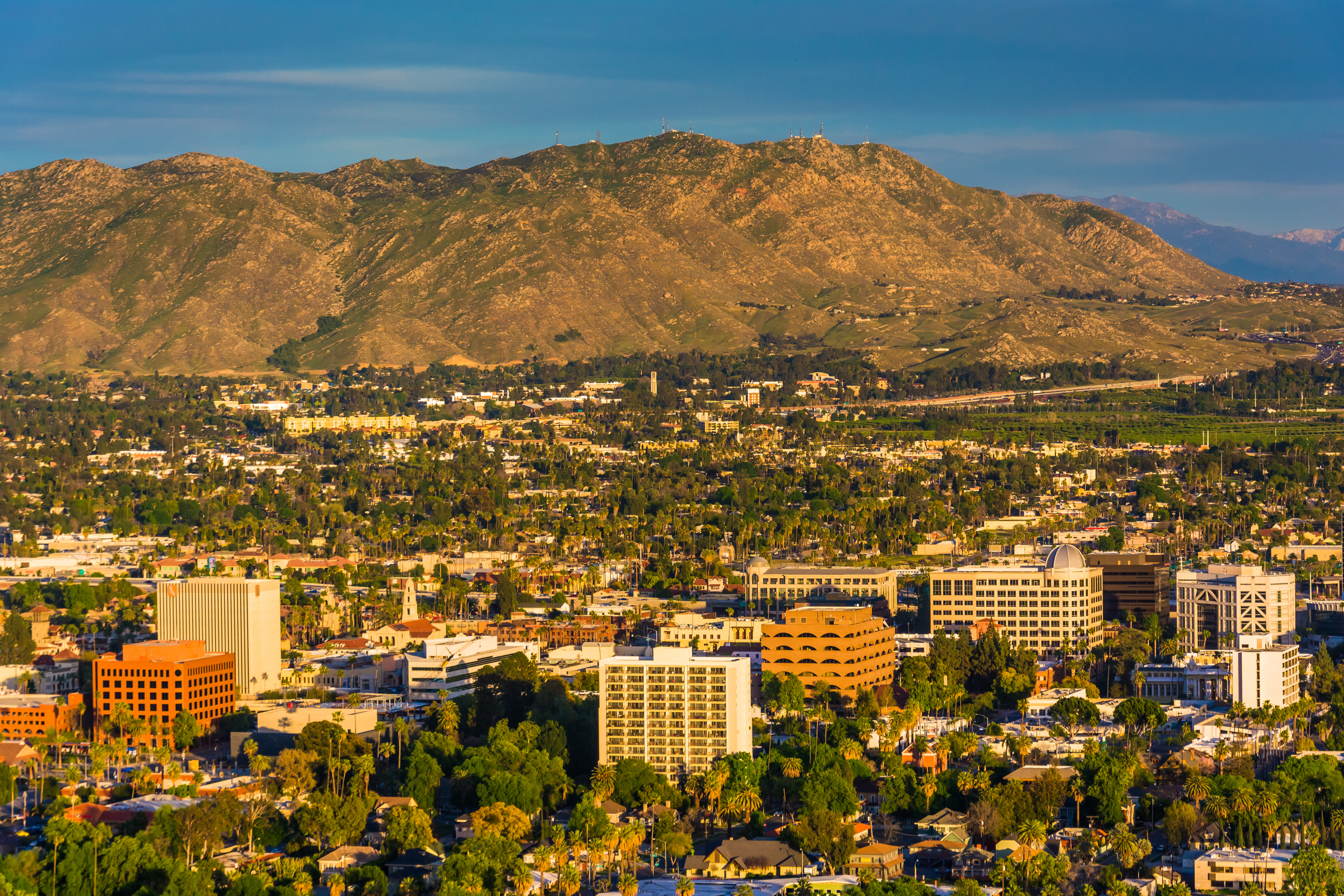 Aerial view of Riverside, CA with buildings in the foreground and mountains in the background.