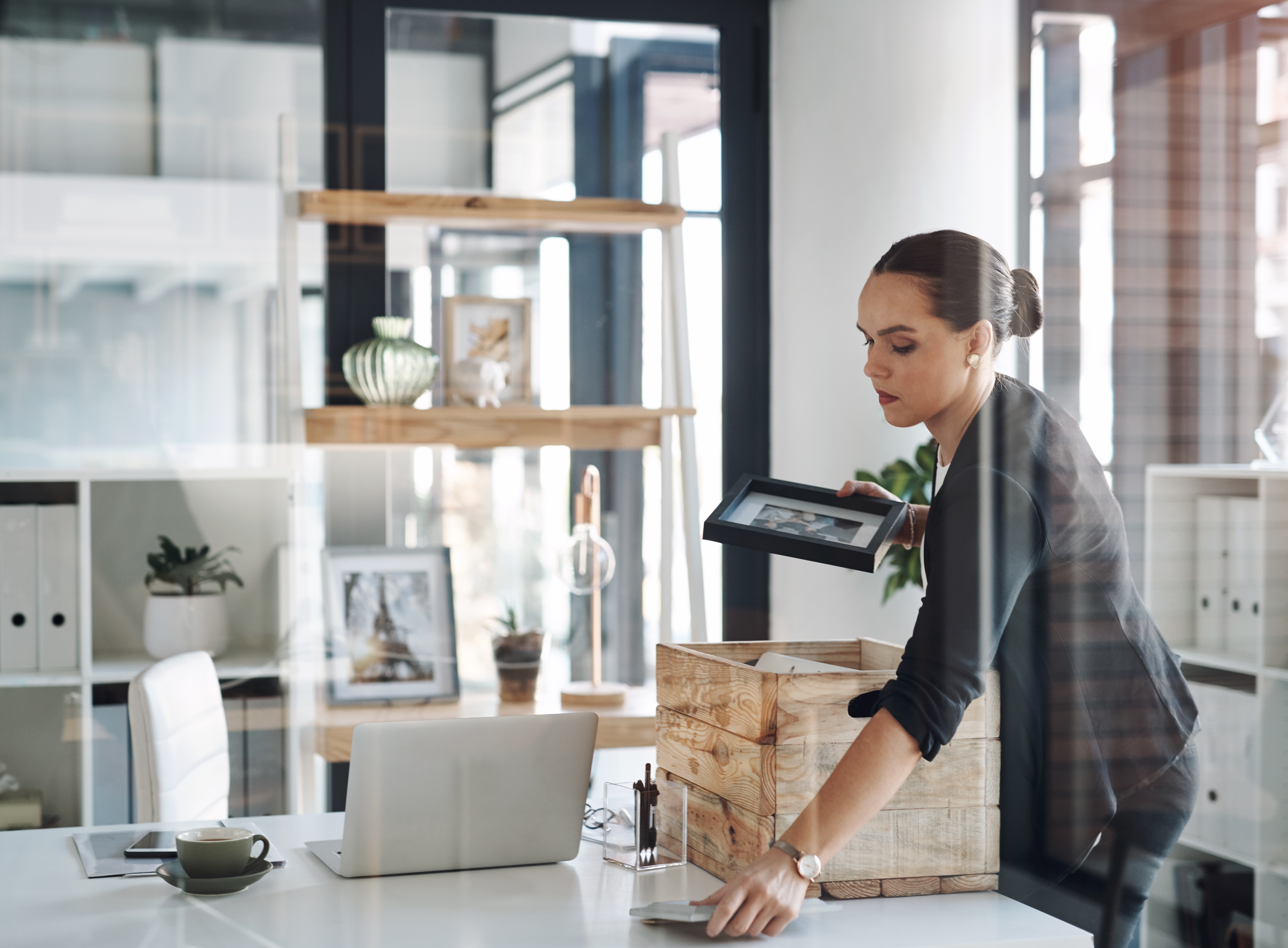 A woman packing belongings in a box on a desk in an office.