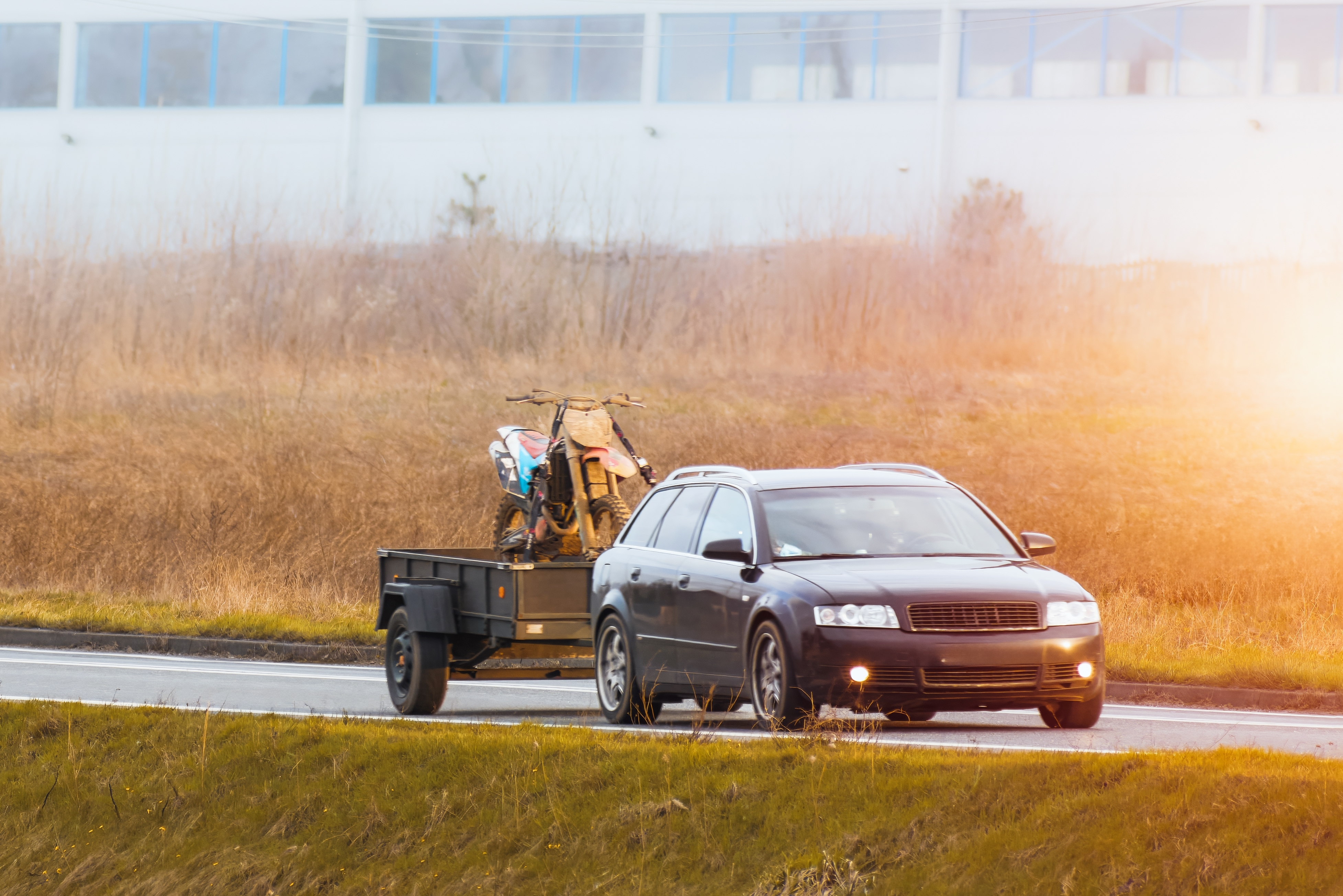 A car on the road with a tow trailer behind it carrying a motorcycle