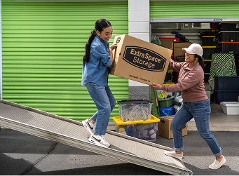 Mother and daughter carrying box from moving truck to storage unit