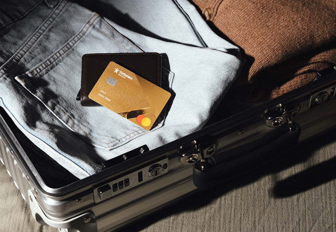 Une valise est ouverte avec quelques vêtements et la carte bancaire gold mastercard de Fortuneo pour partir en voyage.