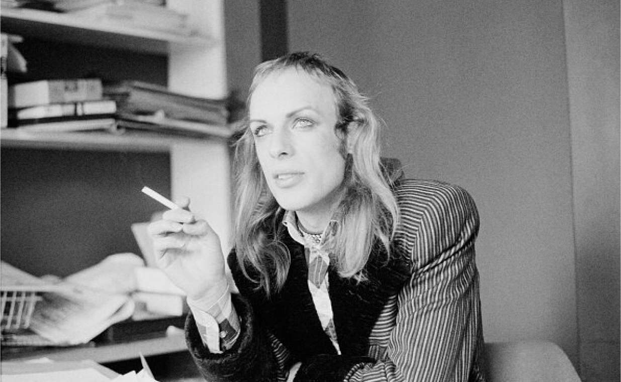 Brian Eno sitting in an office with a cigarette, looking into the distance