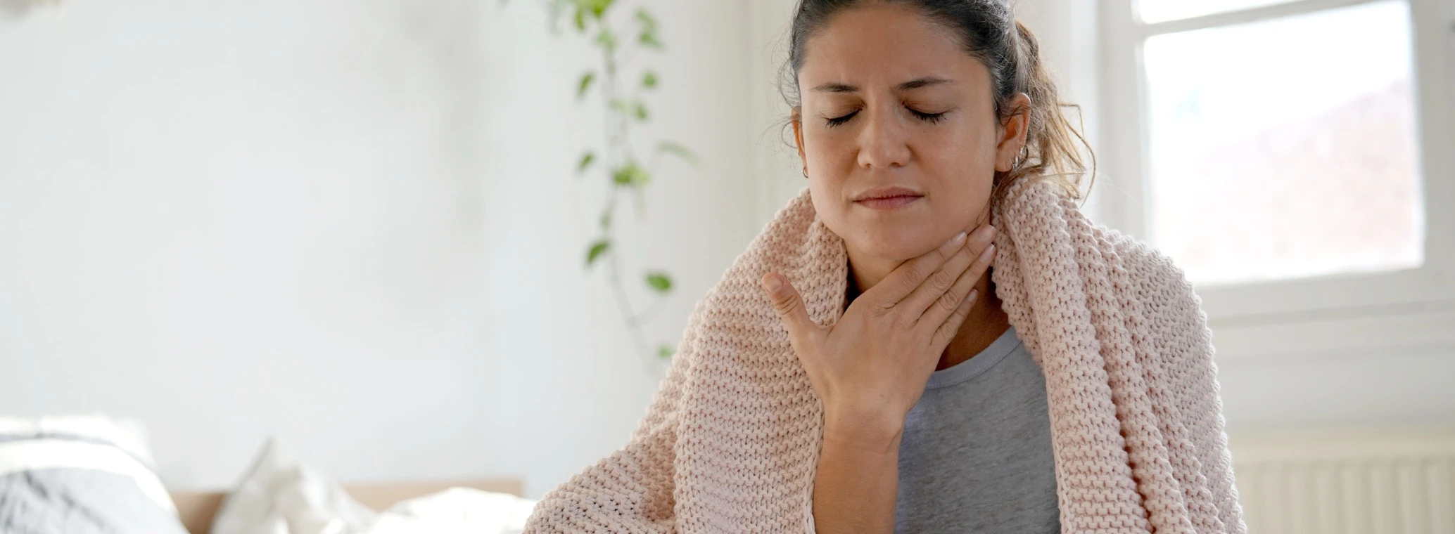 Woman sitting on bed with sore throat