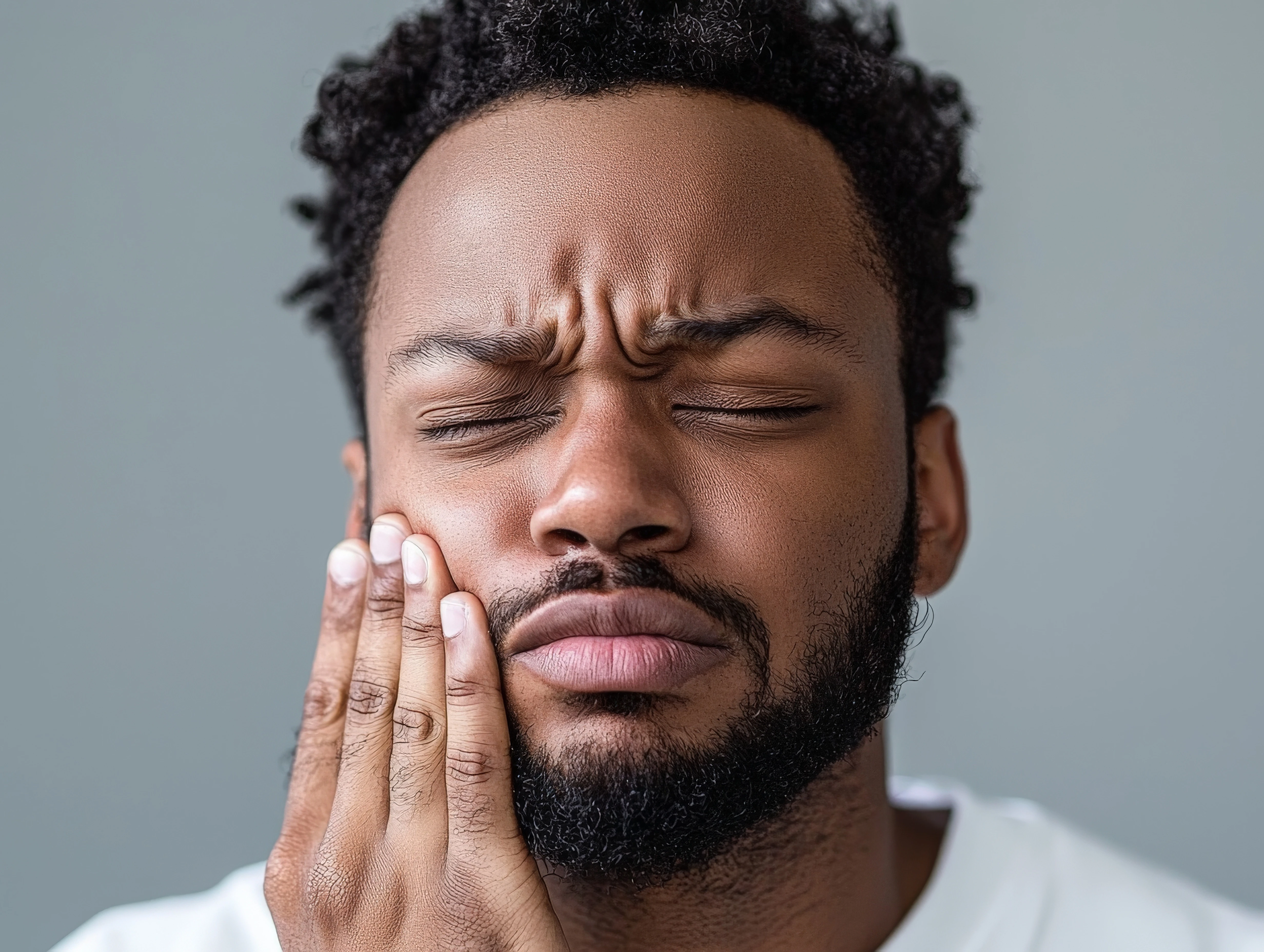 Man holding his jaw and frowning like he is in pain 