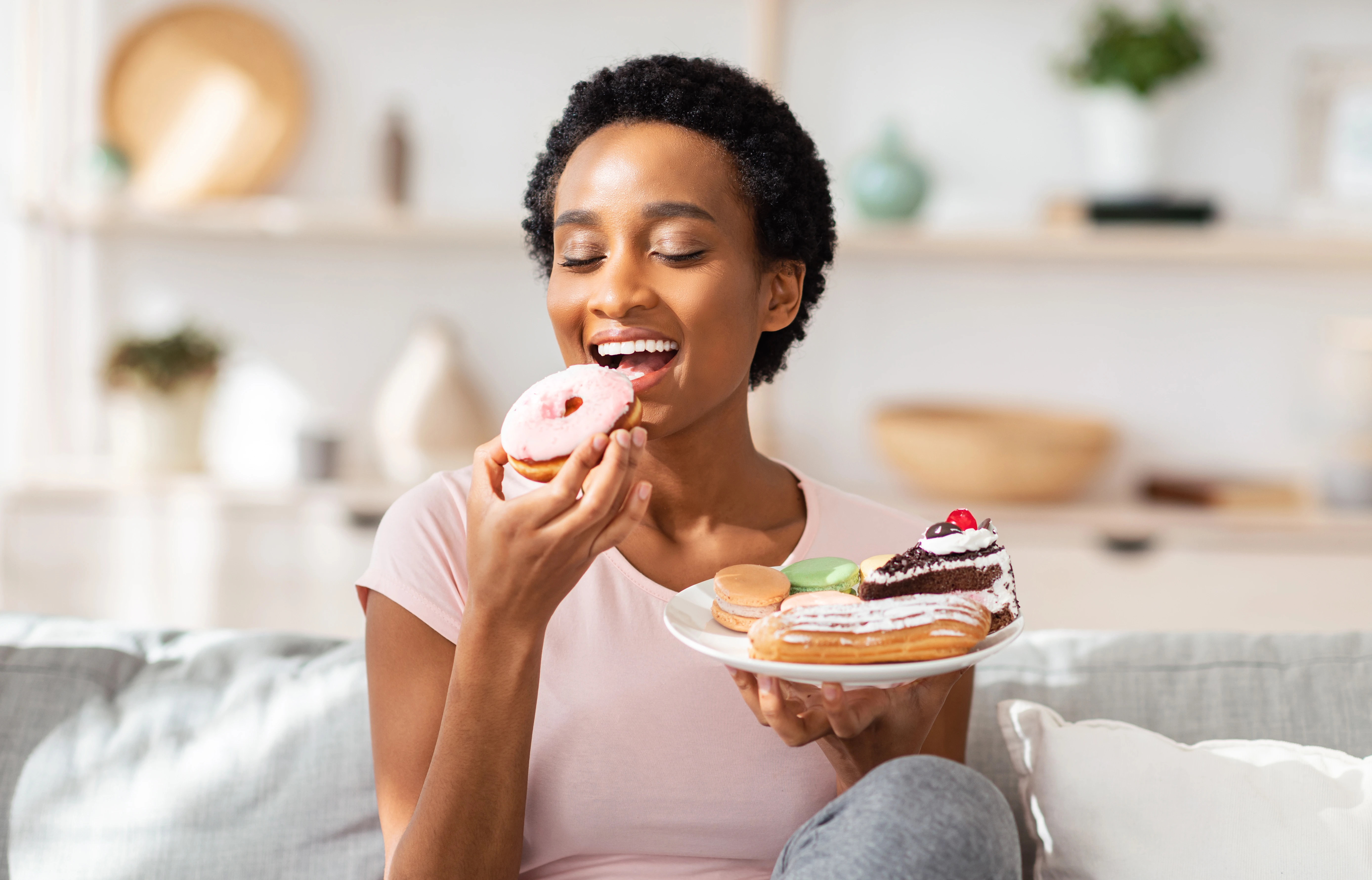A person eating a donut and holding a plate of desserts | Crest