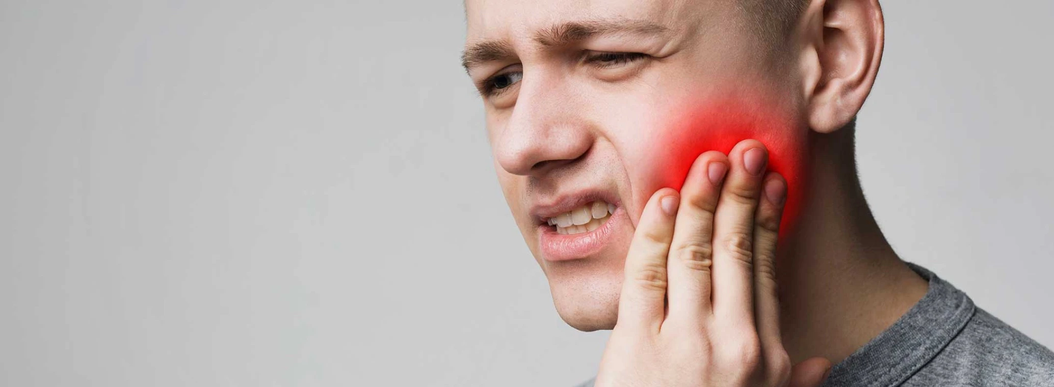 Frustrated young man touching the side of his jaw and frowning