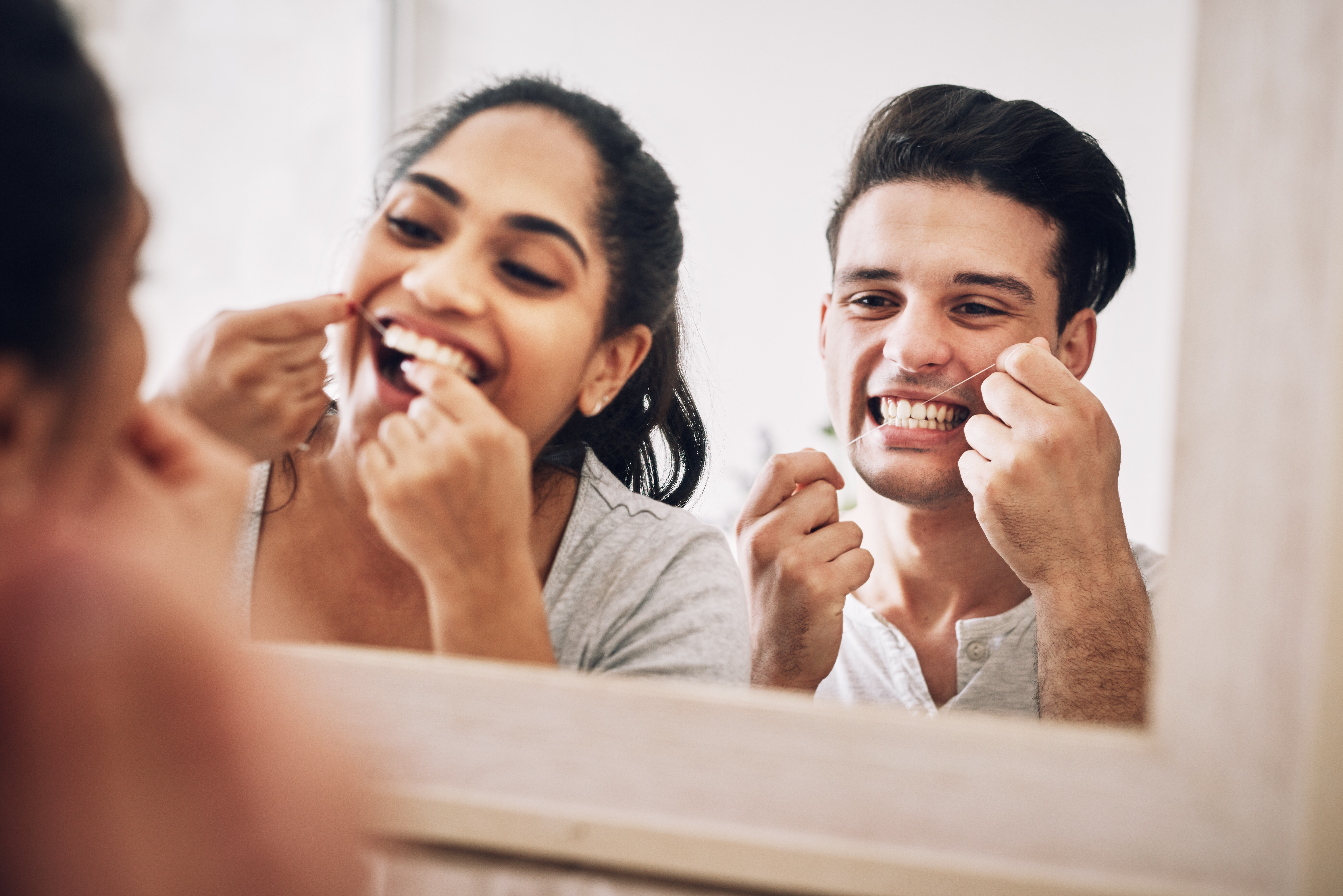 Couple flossing teeth in front of mirror
