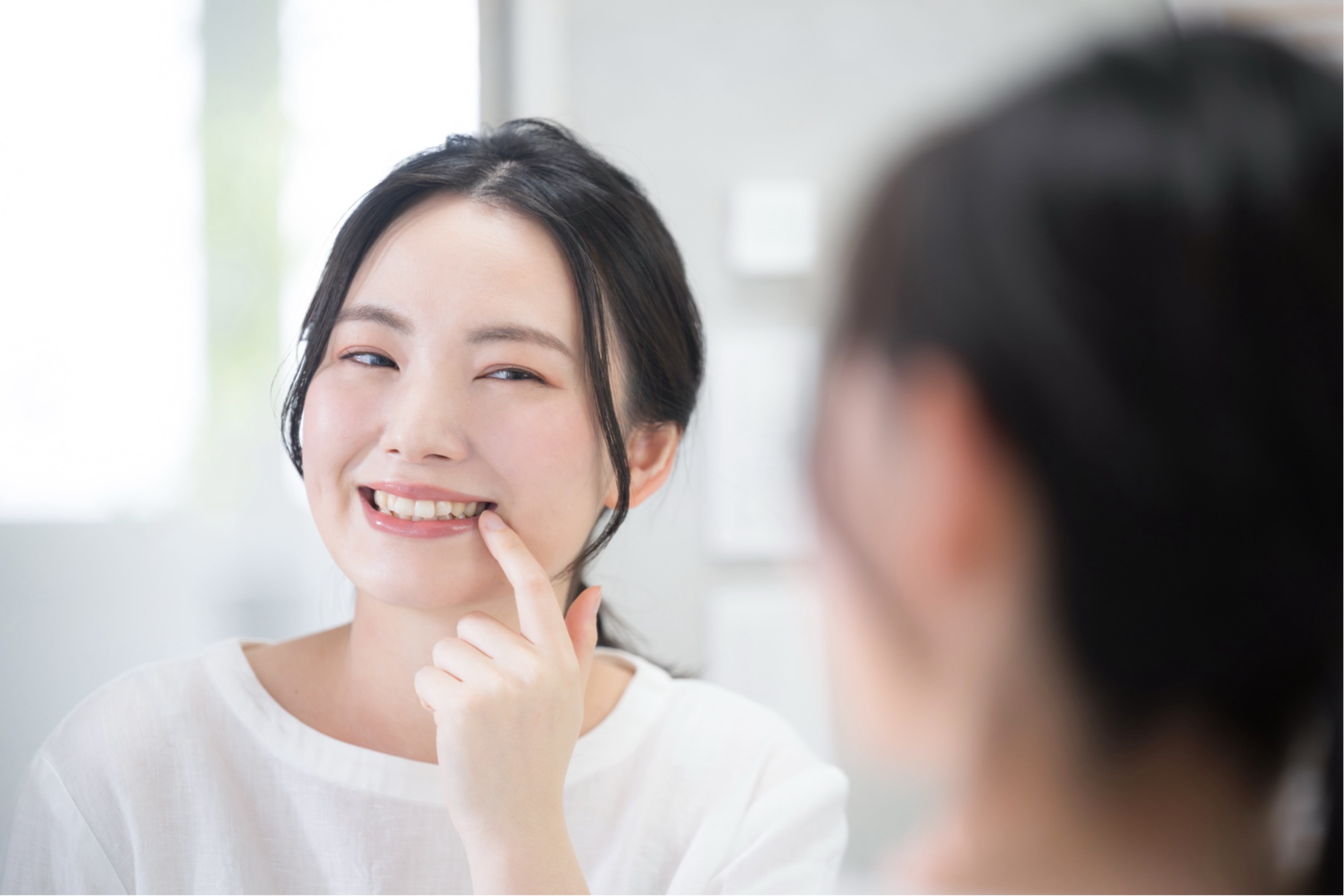 A person smiling at a reflection of themselves in the mirror while pointing at a tooth  | Crest 
