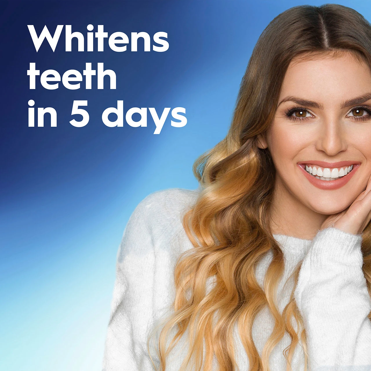 Close-up portrait of a smiling woman in a white sweater with long, wavy light-brown hair, showing bright white teeth. Blue gradient background with bold white text reading "Whitens teeth in 5 days."