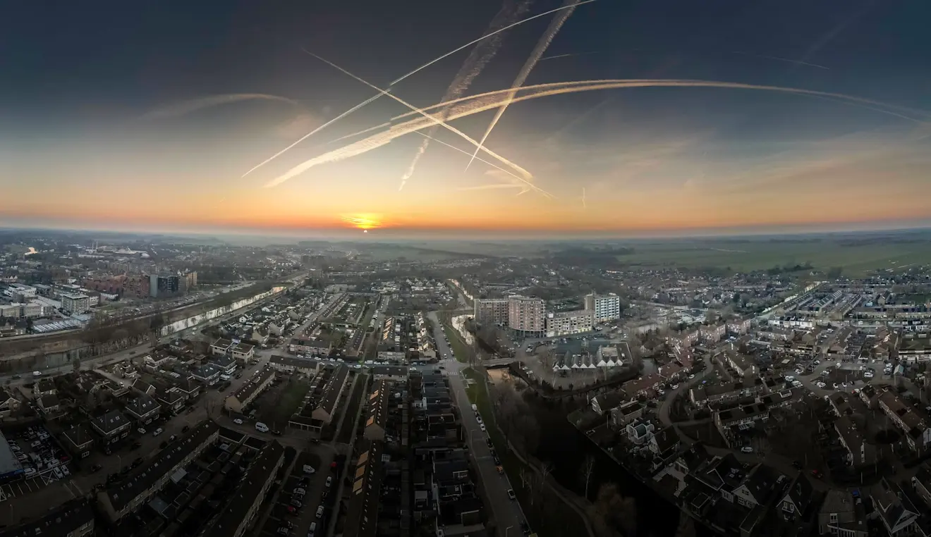 Zonsondergang boven Leerdam, met veel vliegtuigstrepen in de lucht - John Oomen