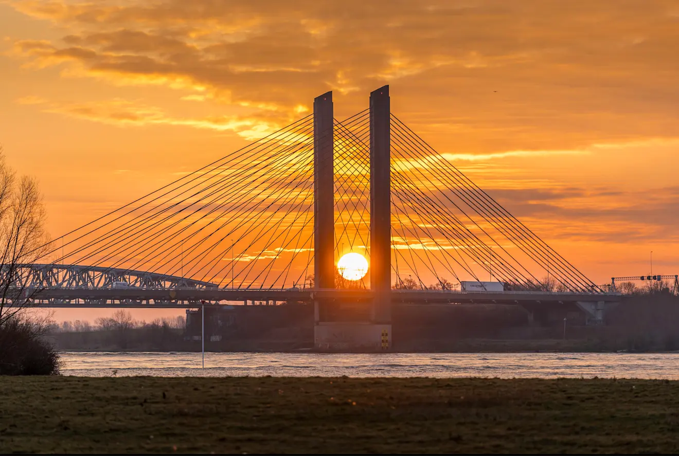 De zon precies tussen de pijlers van de brug - John Oomen