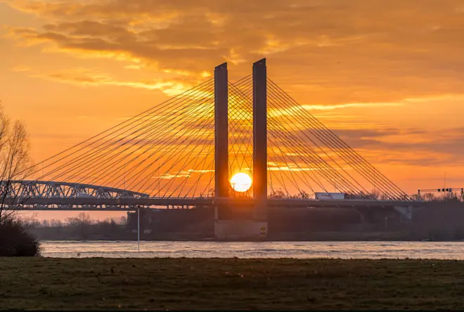 De zon precies tussen de pijlers van de brug - John Oomen