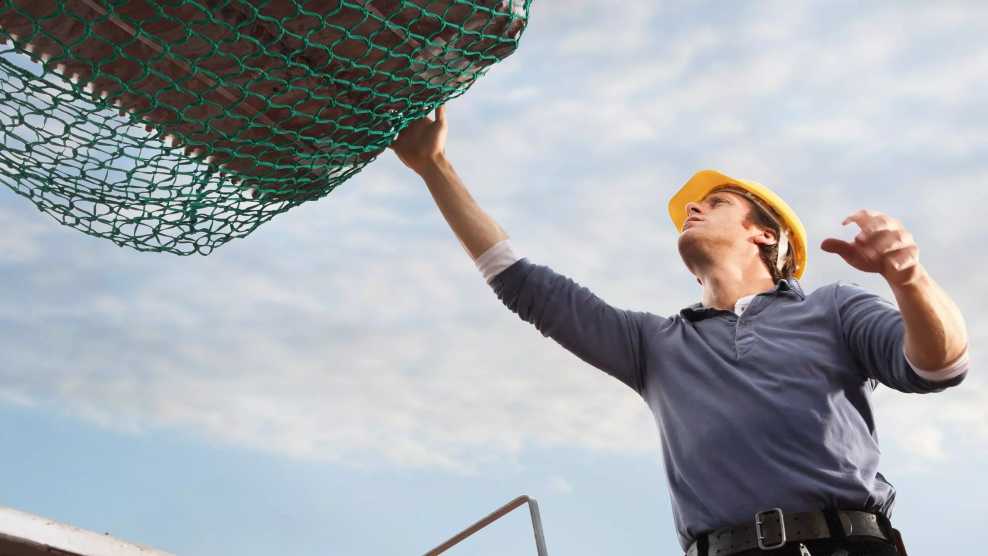 Ein Verarbeiter auf einem Dach nimmt Arbeitsmaterial entgegen.