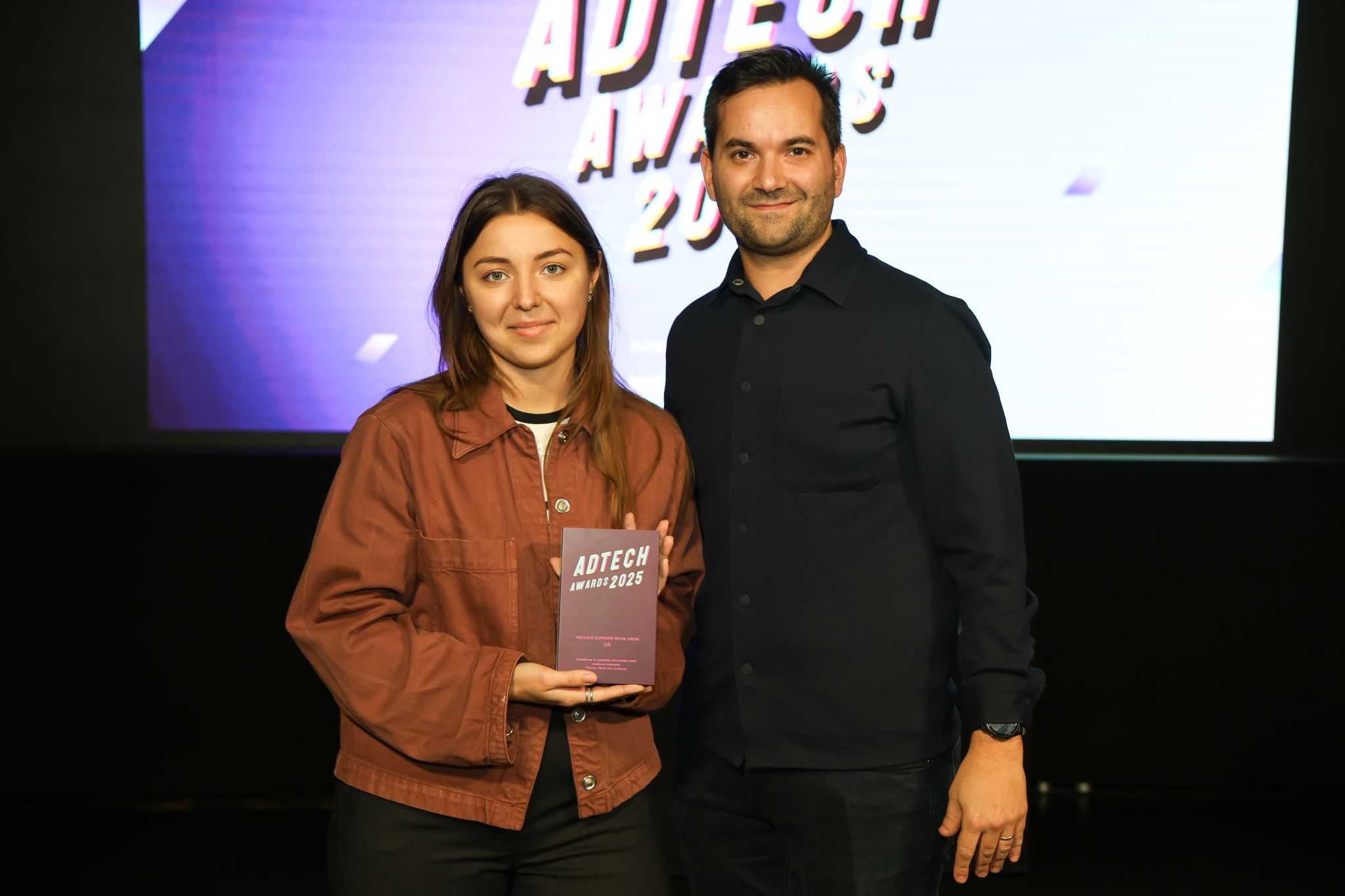 Kristina Raptovaia (left), Head of Partnerships and Advertising/Retail Media Lead at Rakuten France, and Arnaud Cappelaere (right), Strategy and Customer Success Manager at Mirakl Ads, pose together at the 2025 Adtech Awards. Kristina holds a purple award plaque for "Meilleur Dispositif Retail Media - Or" (Best Retail Media Campaign - Gold) against a backdrop featuring the event's logo.
