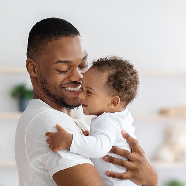 Homme souriant tenant son bébé dans ses bras.