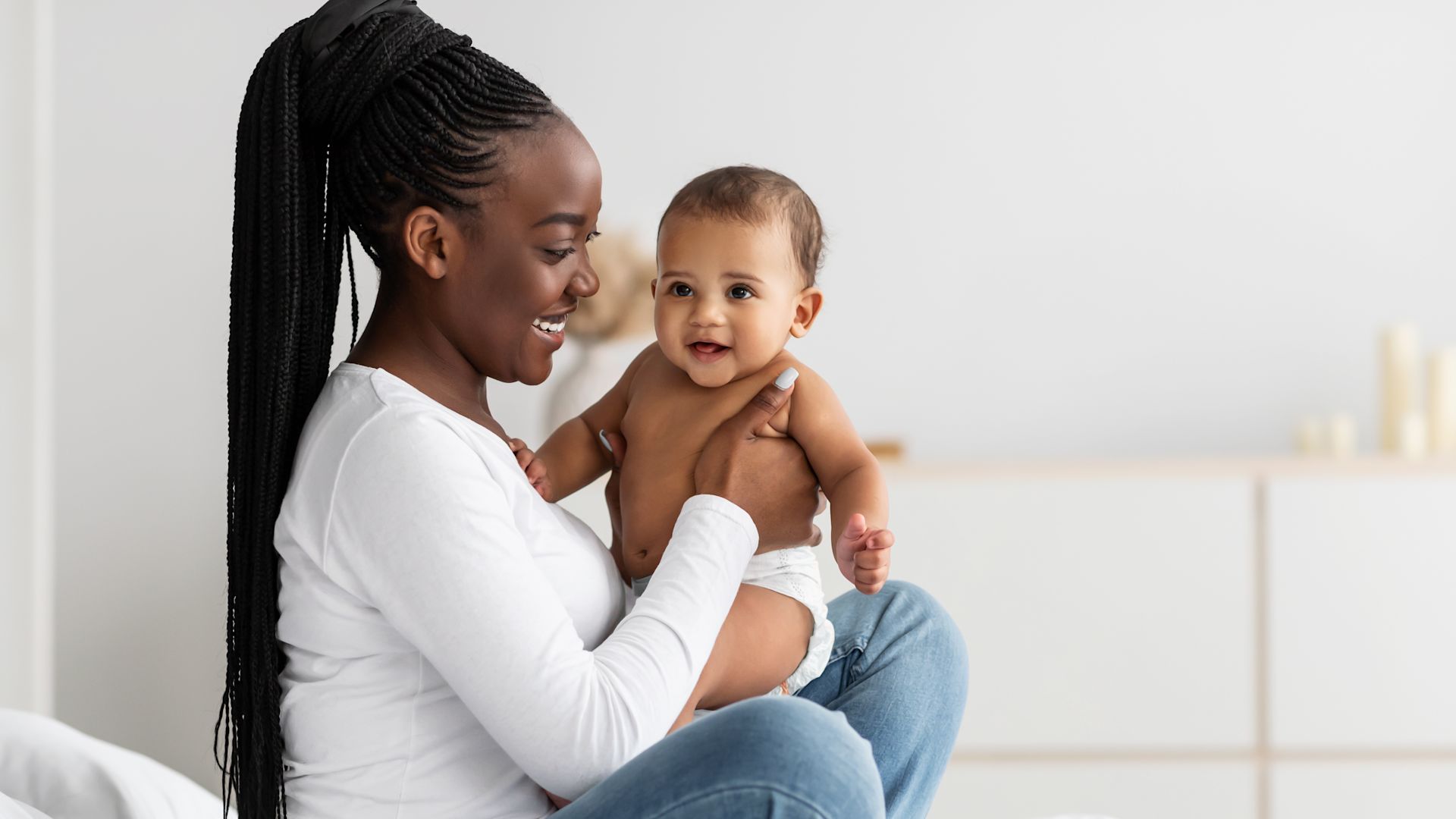 Woman sitting on a bed, holding and smiling at her baby