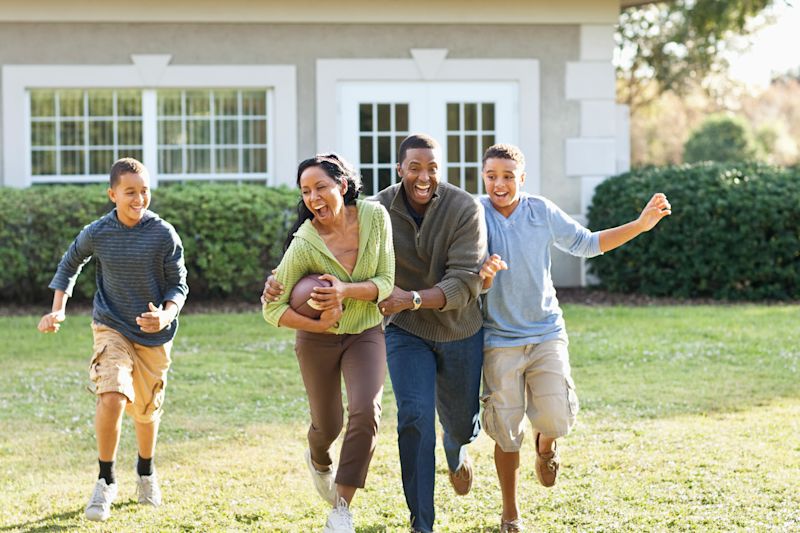 Happy family playing football together in front of their home.