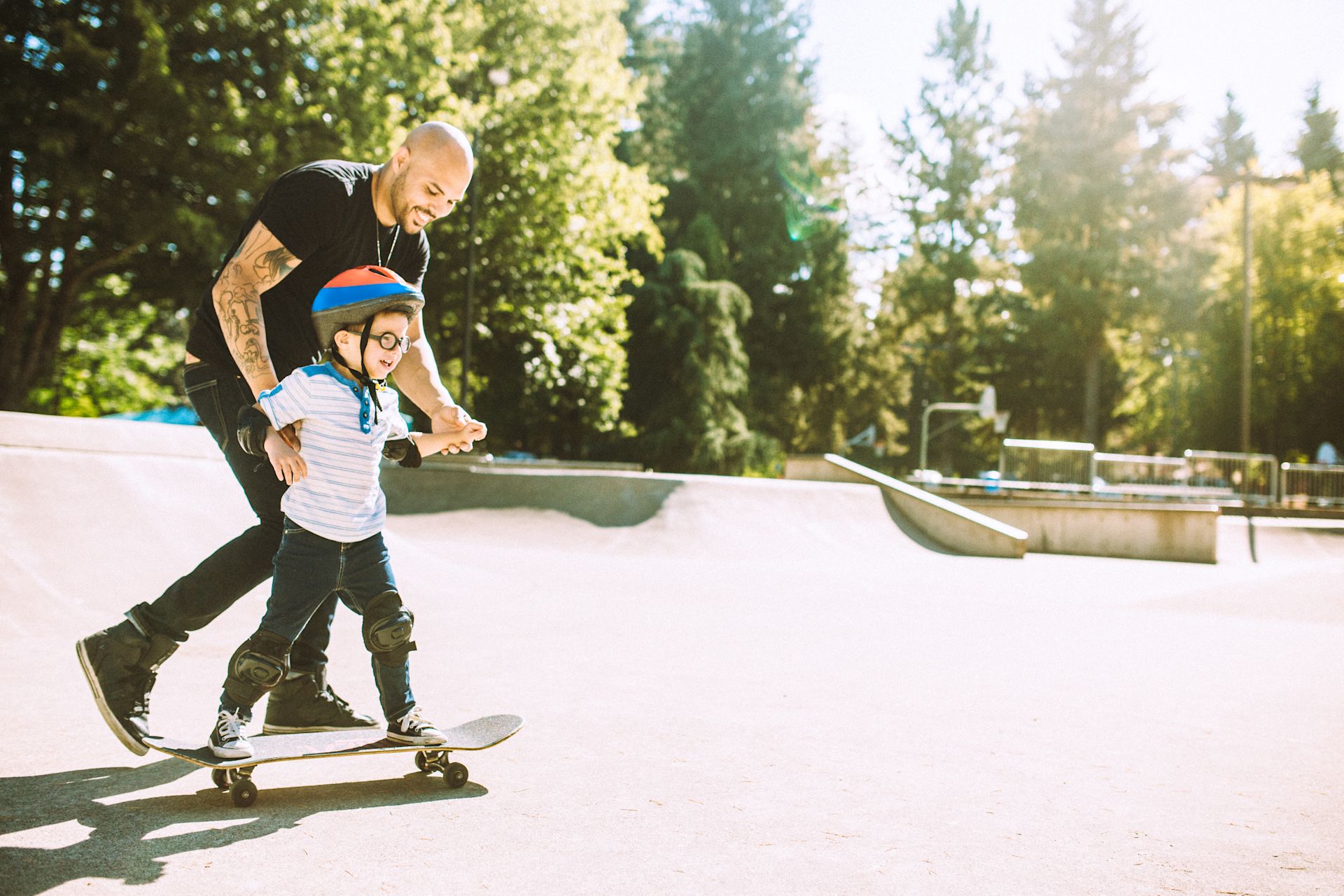 Father teaching his young son to skateboard in a park.