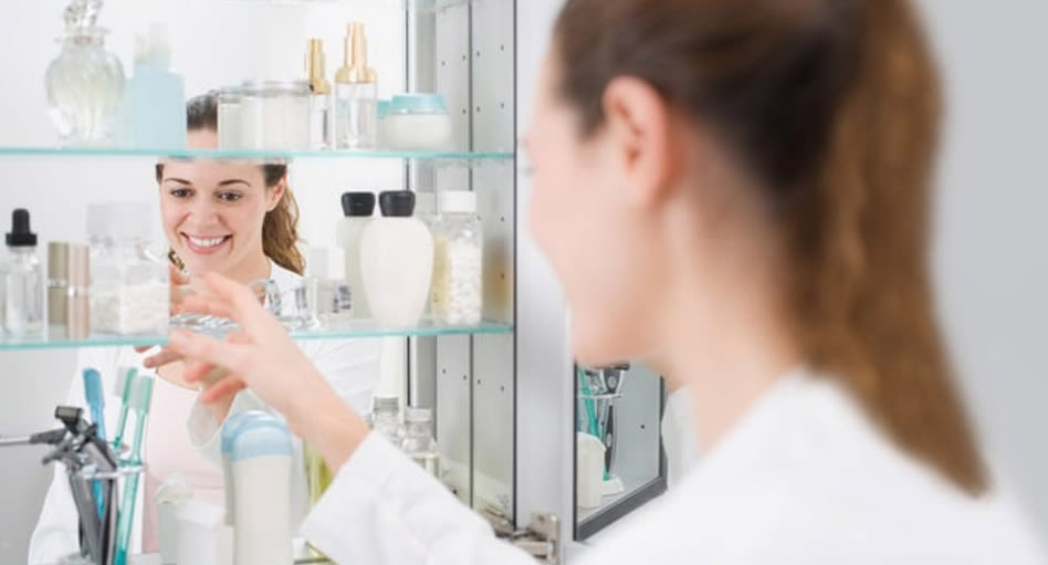 Femme qui cherche un pot de Tylenol dans une armoire avec miroir.