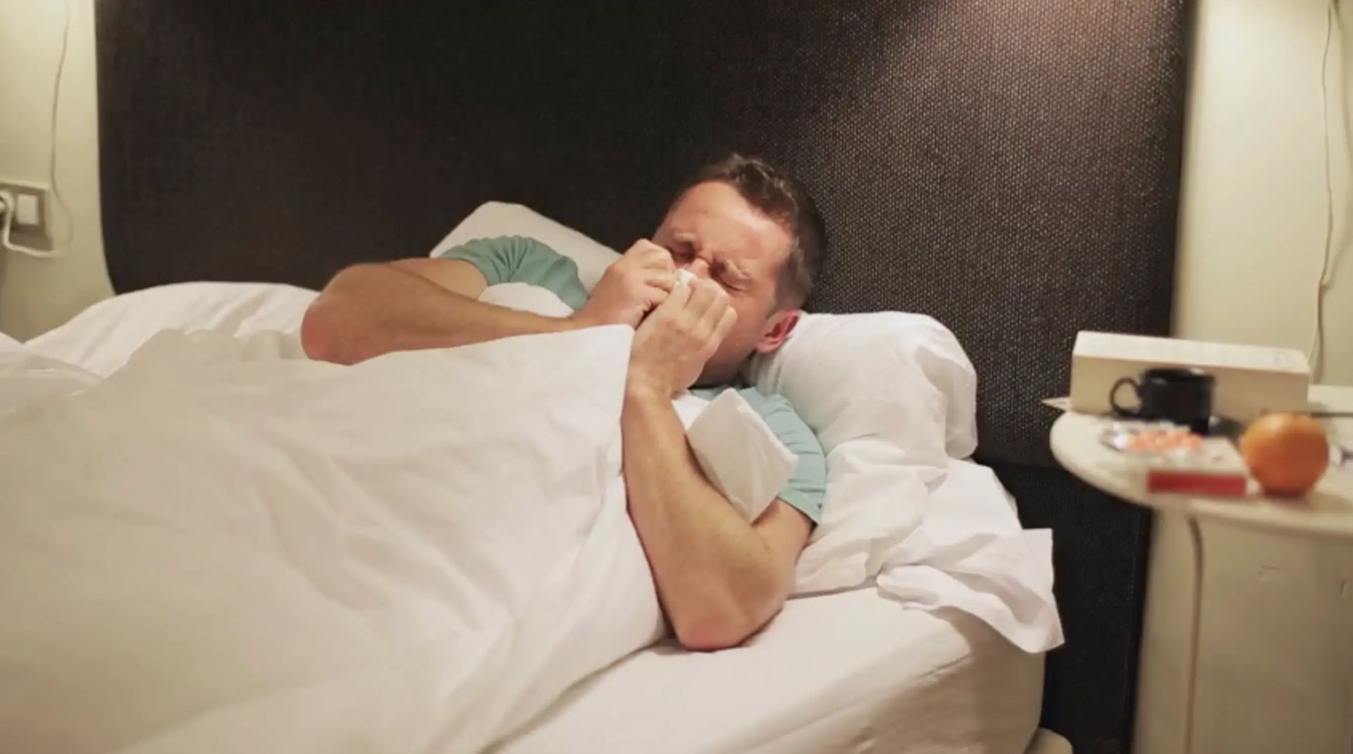 Man sneezing in bed