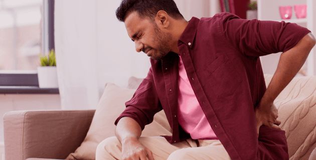 Hombre sentado en el sofa con dolor de espalda