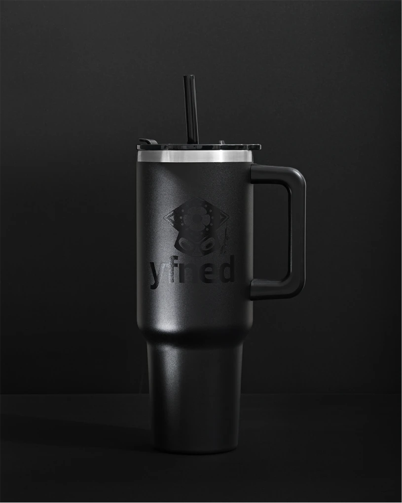 Matte black travel mug with handle and straw, embossed with YFNED logo, on a black background.