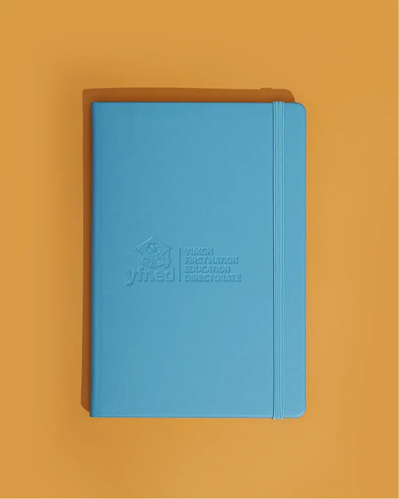 Light blue notebook with elastic band and embossed YFNED logo and ‘Yukon First Nation Education Directorate’ text.
