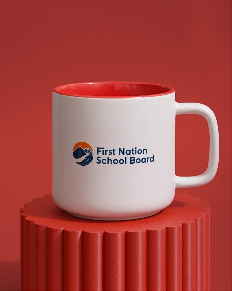 White ceramic mug with red interior and First Nations School Board logo on front, on a red background.