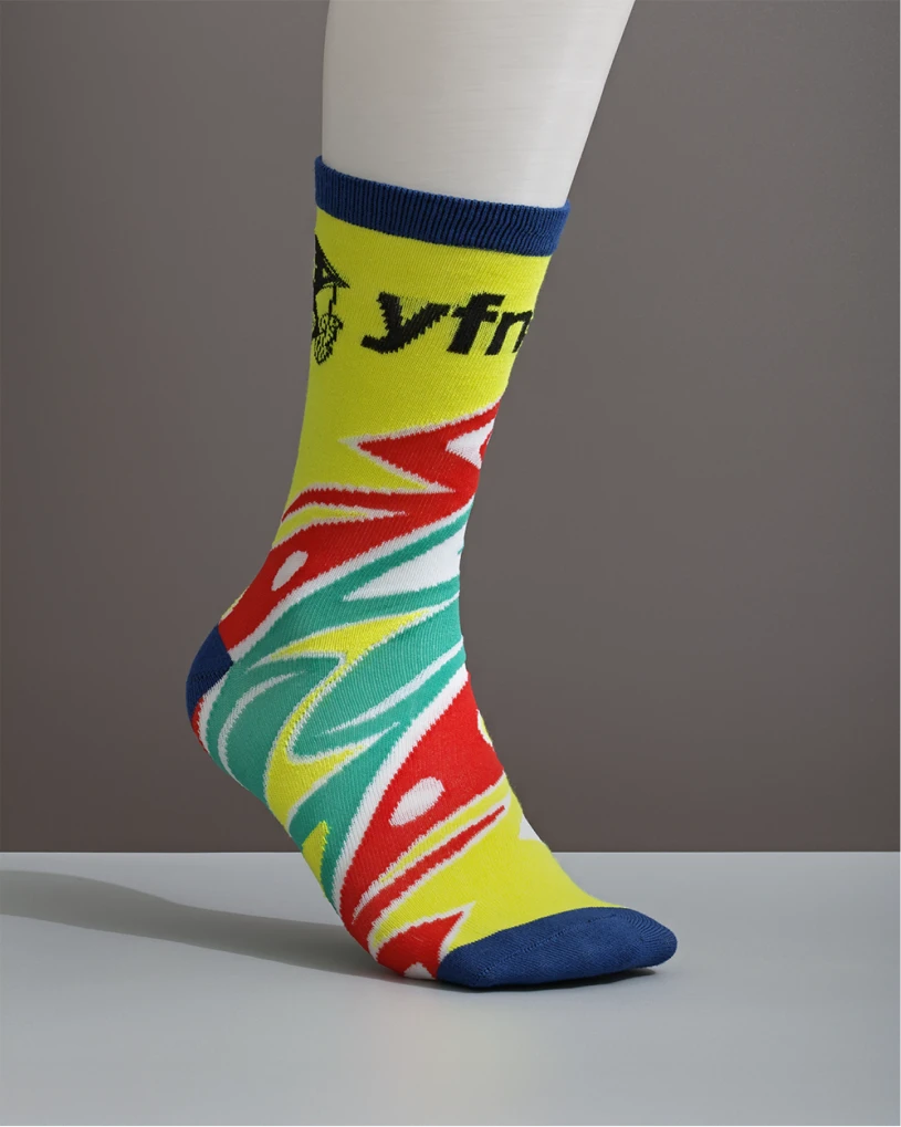 Foot wearing colourful YFNED crew sock with yellow, red, teal, and blue pattern and logo near cuff.