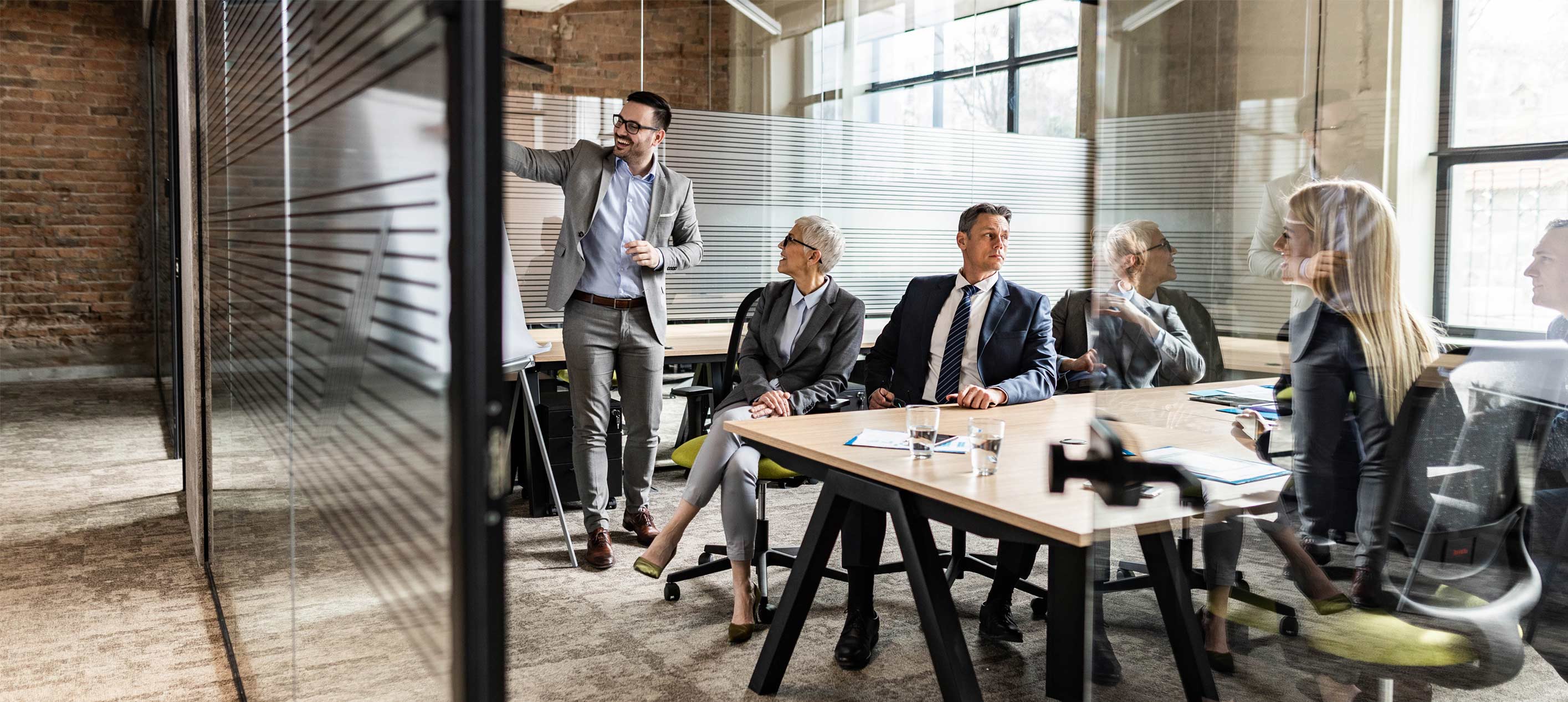 Professional business meeting in a modern office with a presenter leading a discussion while colleagues are seated around a desk.