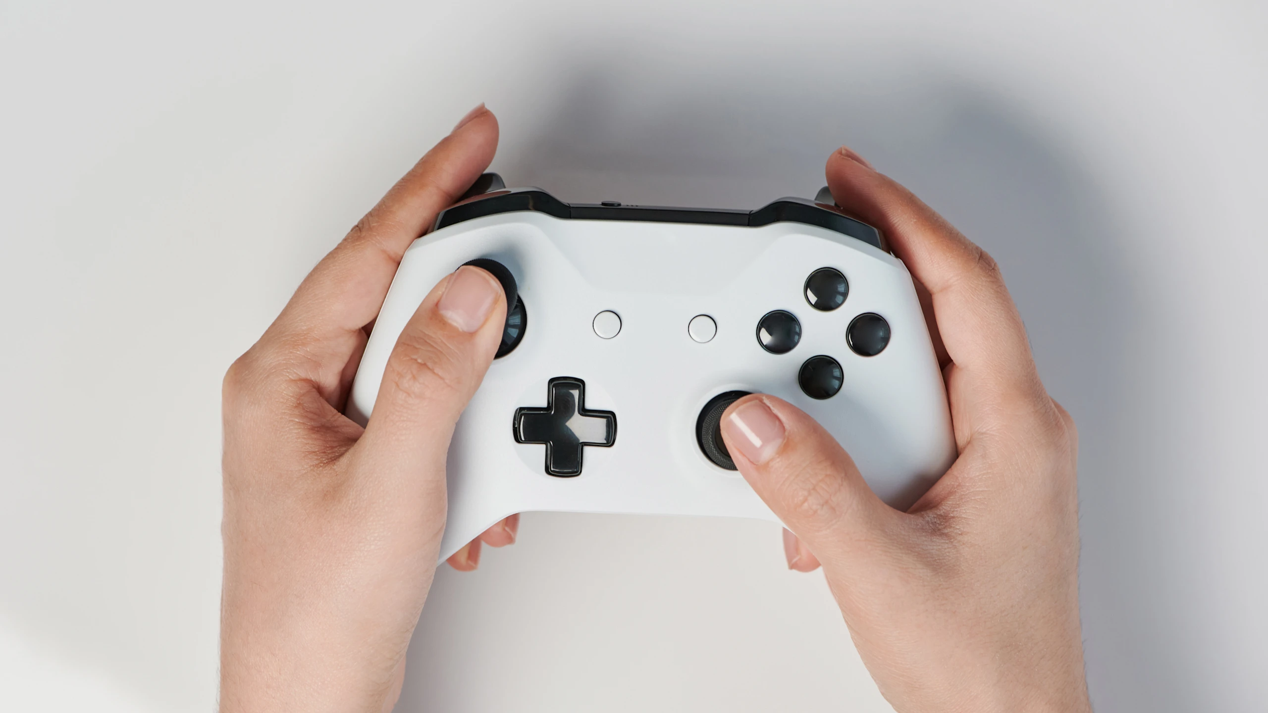 A pair of hands holding a white video game controller with black buttons against a plain light background.