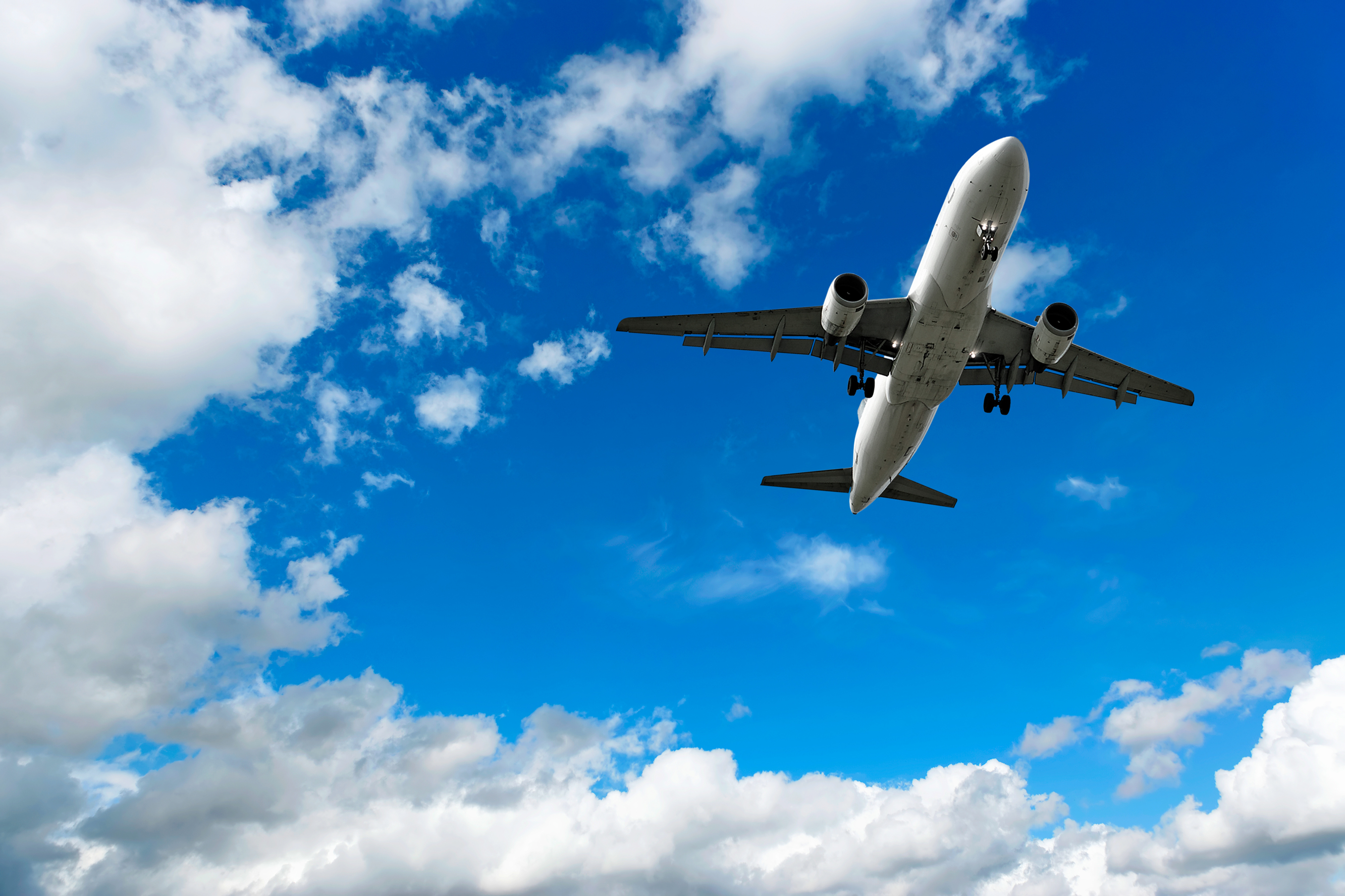 Commercial airplane flying low against a blue sky with scattered white clouds, viewed from below.
