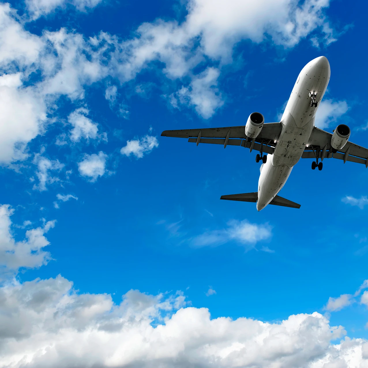 Commercial airplane flying low against a blue sky with scattered white clouds, viewed from below.