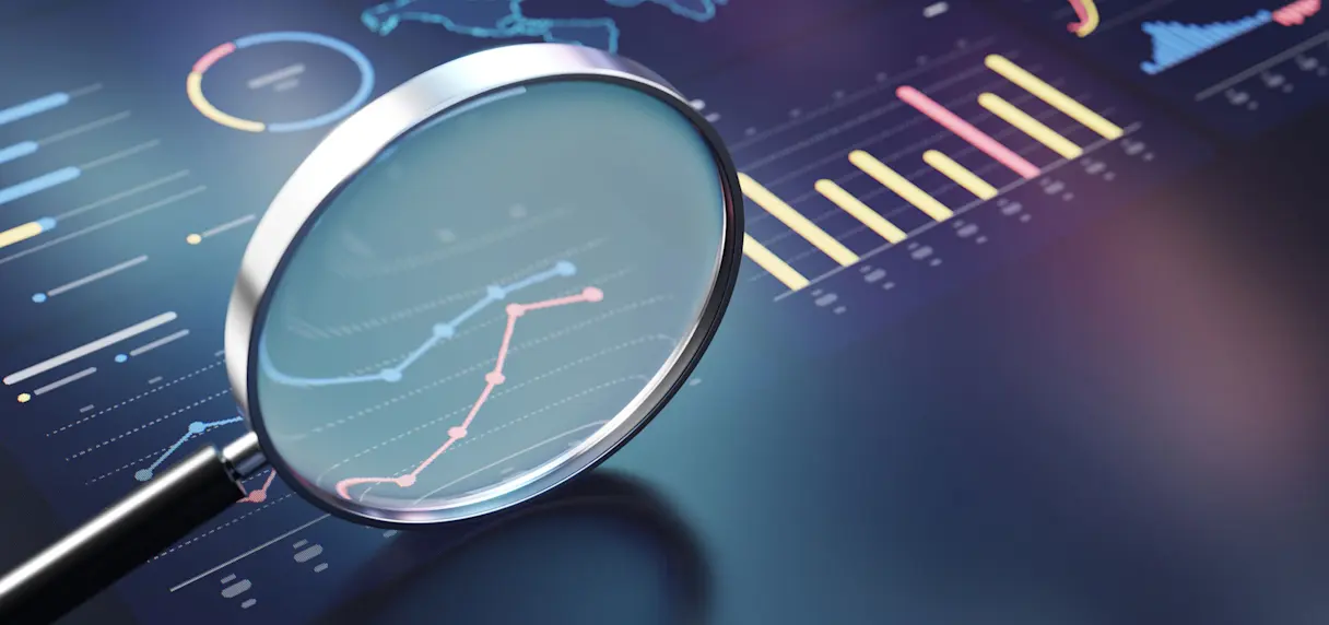 A magnifying glass over a digital dashboard displaying line graphs and bar charts on a dark blue background.