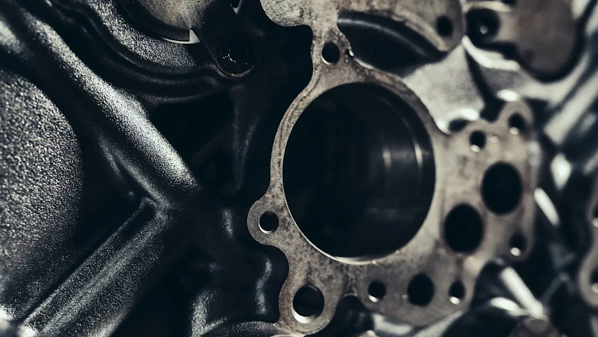 Close-up of a metal engine gasket with bolt holes, surrounded by dark, machined metal components and gears.