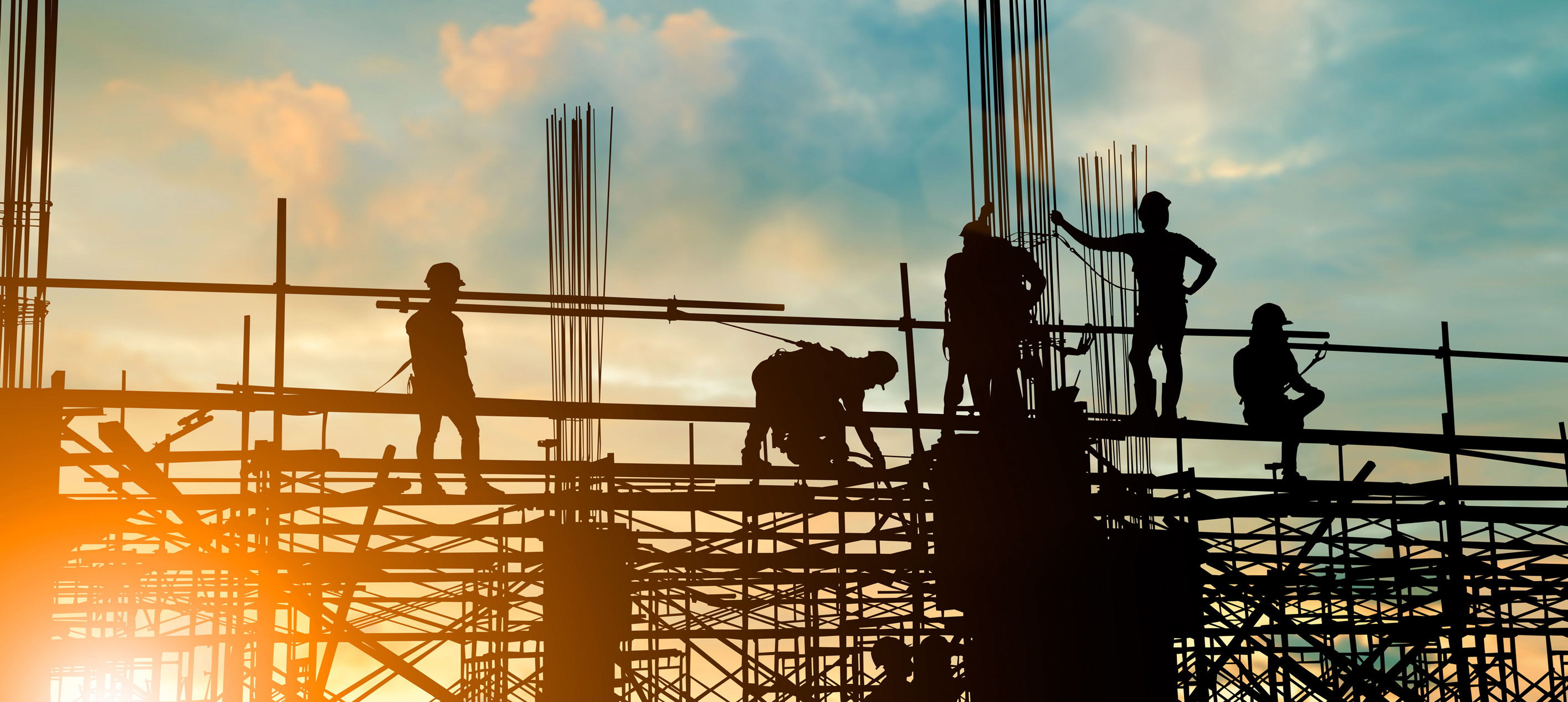 construction workers and engineers working on scaffolding against a sunset sky.