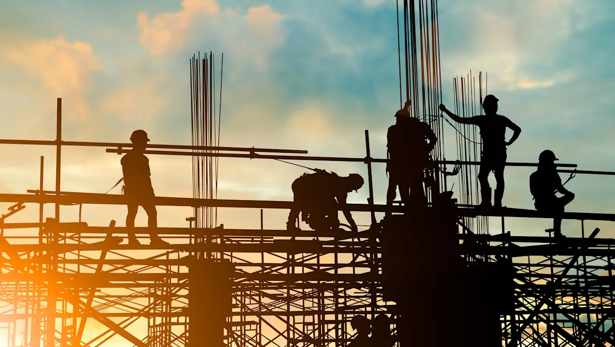 construction workers and engineers working on scaffolding against a sunset sky.