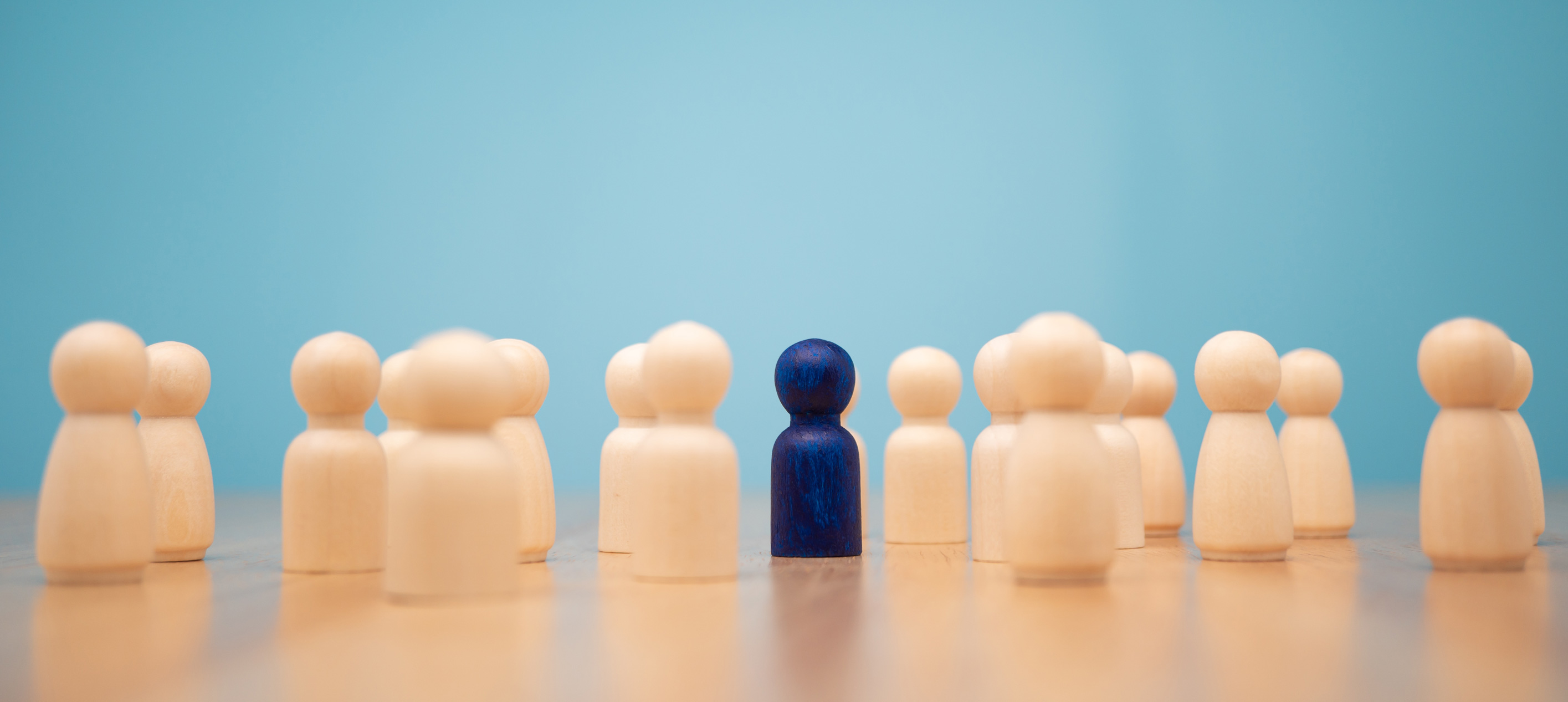 Many Wooden Human Figures With One Standing Out Painted Blue