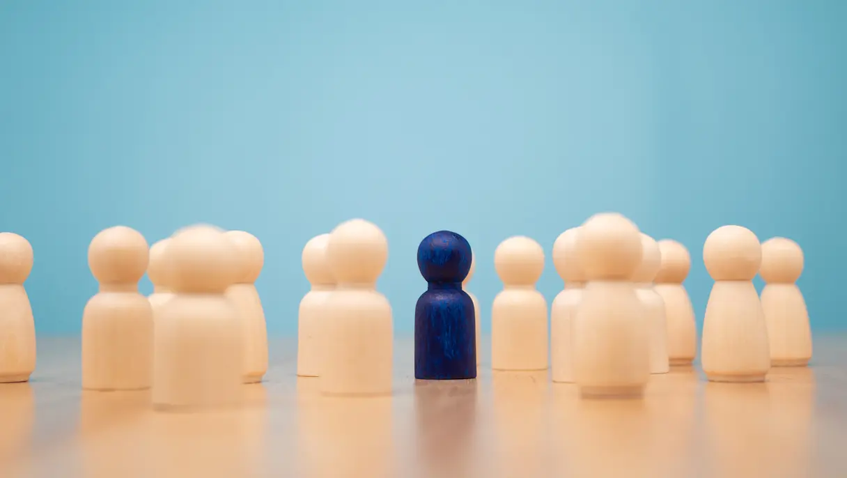 Many Wooden Human Figures With One Standing Out Painted Blue