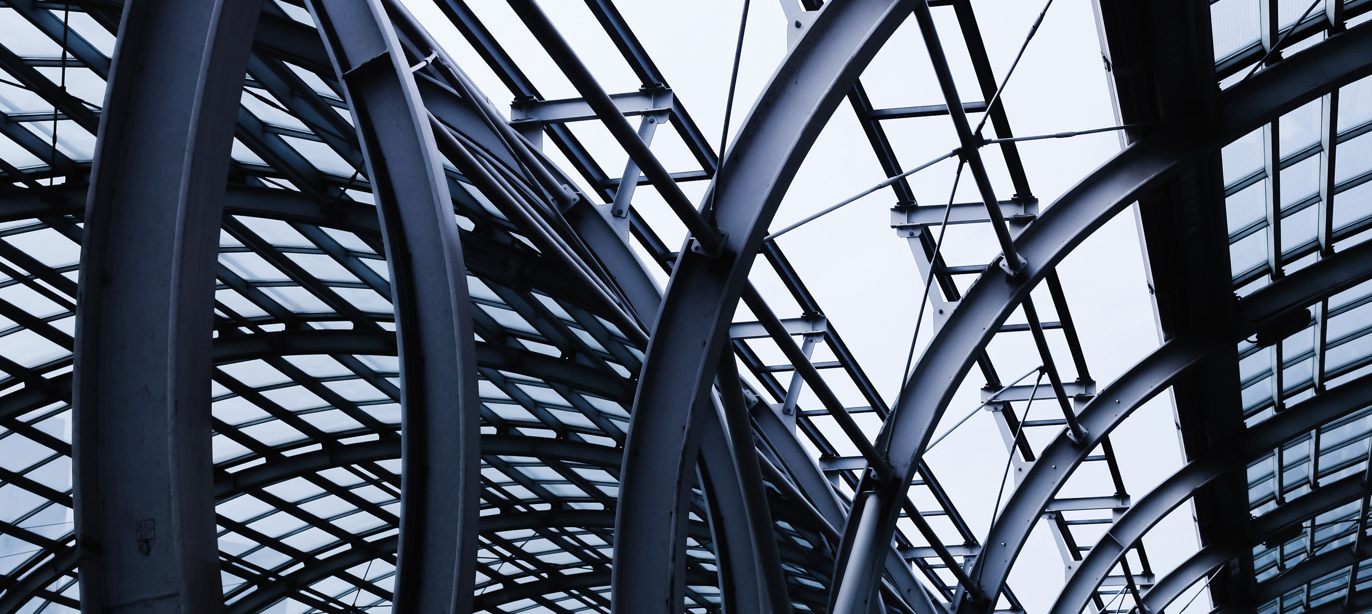 Upward view of a modern glass roof supported by curved steel beams and an intricate geometric framework.