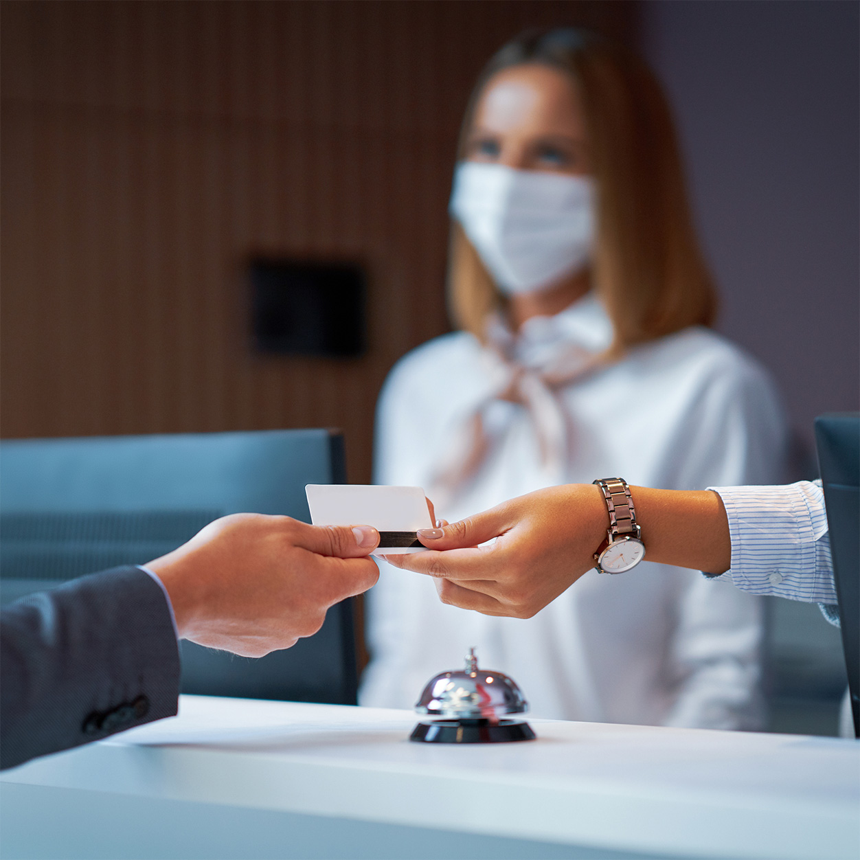 Person Handing Another Person a Card with Masked Woman in Background