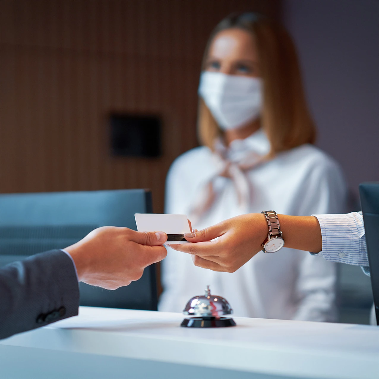 Person Handing Another Person a Card with Masked Woman in Background