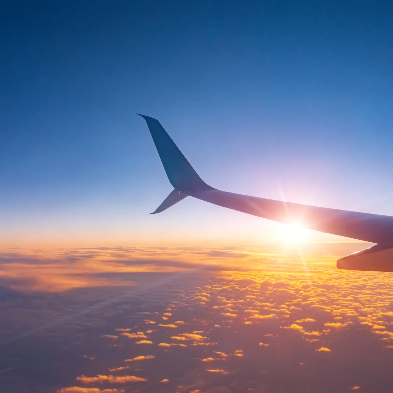 Airplane window at sunset, highlighting the wing and winglet