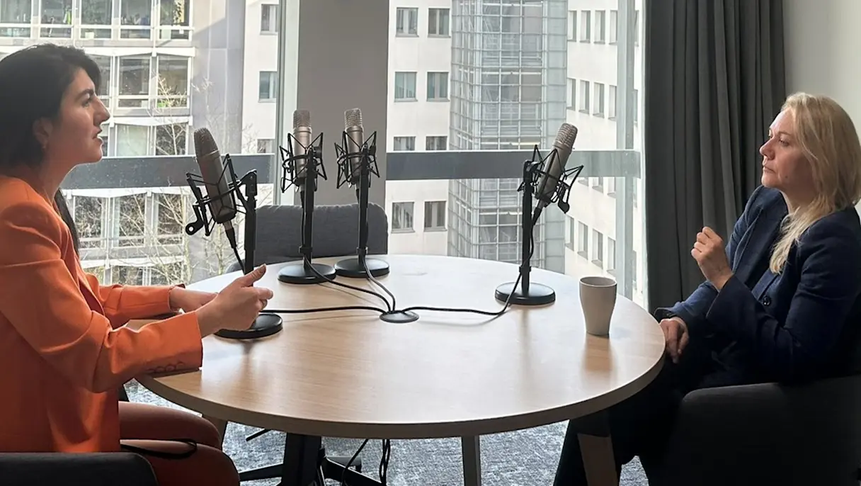 Two professionals sitting across from each other at a table with podcast mics in front of them